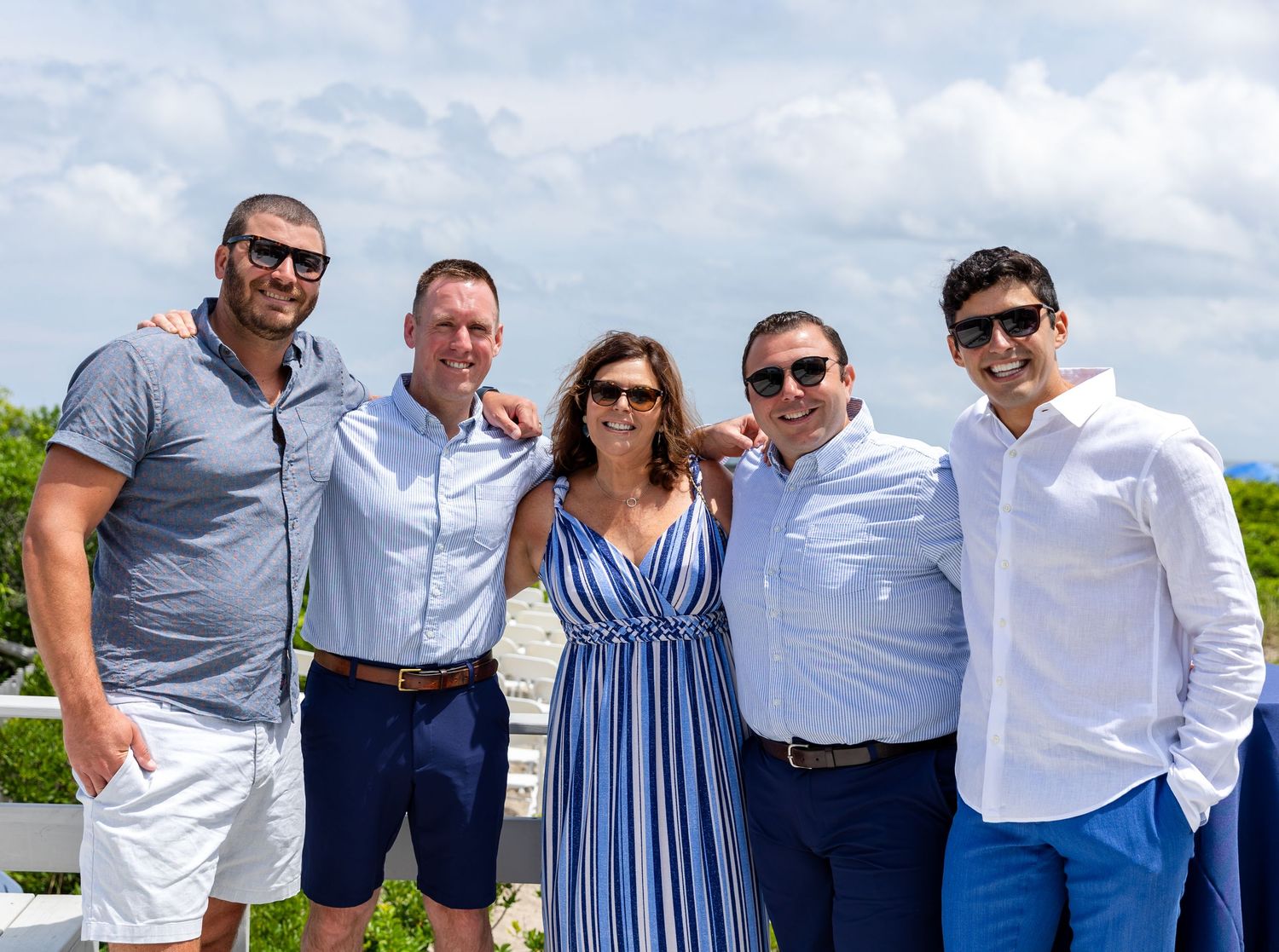 A group stands together outdoors wearing coordinated blue and white outfits on a sunny day near water.