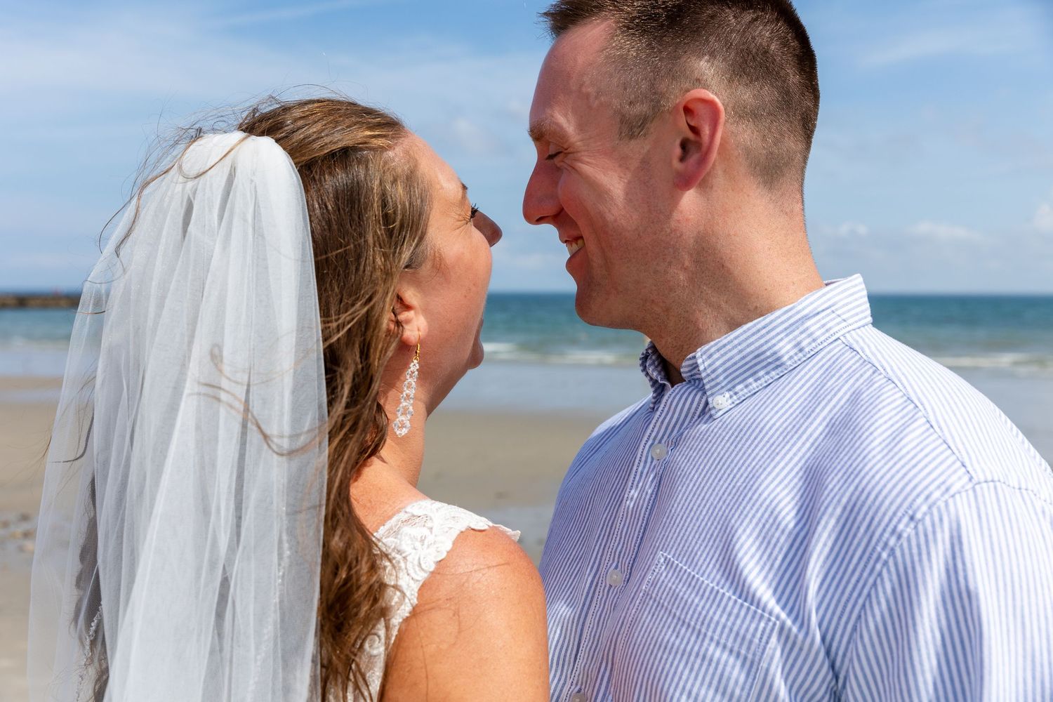A bride and groom share an intimate moment on a sunny beach with turquoise waters and blue skies in the background.