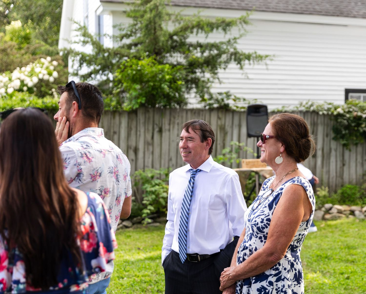 Guests in formal attire mingle and socialize on a green lawn at an outdoor summer event.