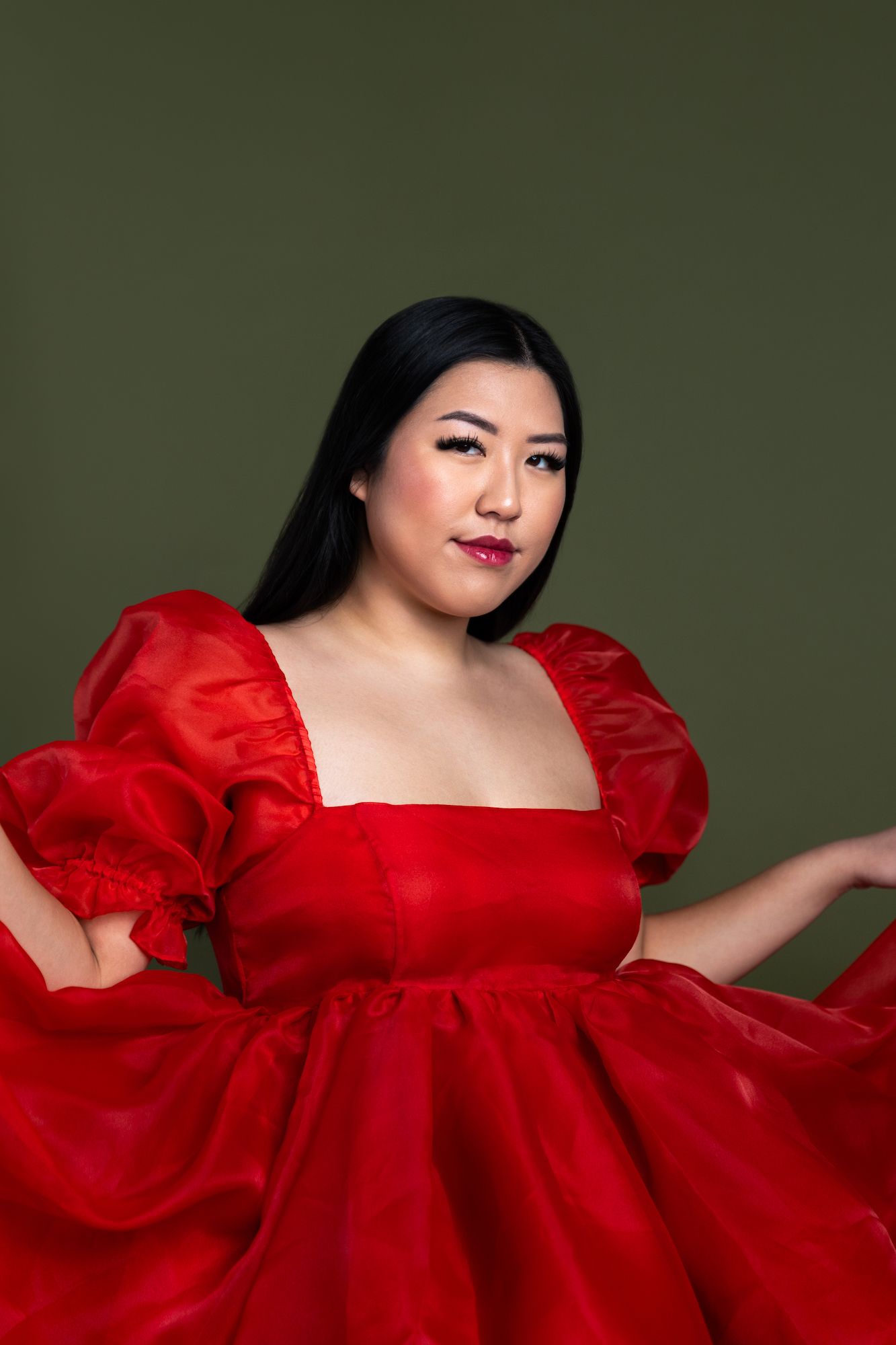 Portrait against dark green background showing elegant red dress with puff sleeves.