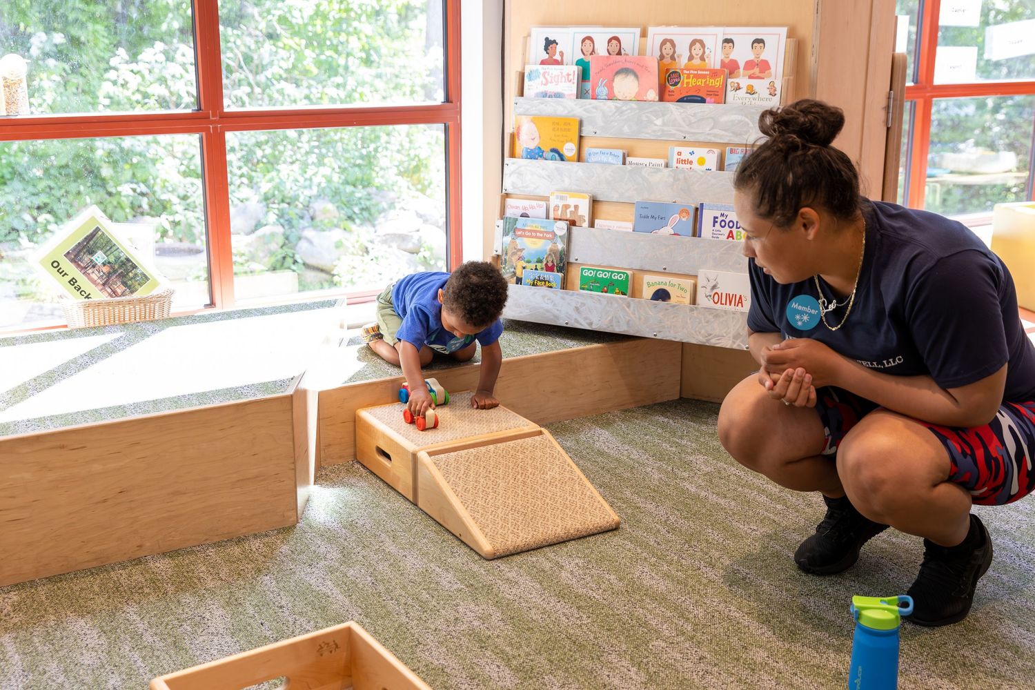 Student and instructor working with educational materials in a bright classroom setting with learning displays on the wall.