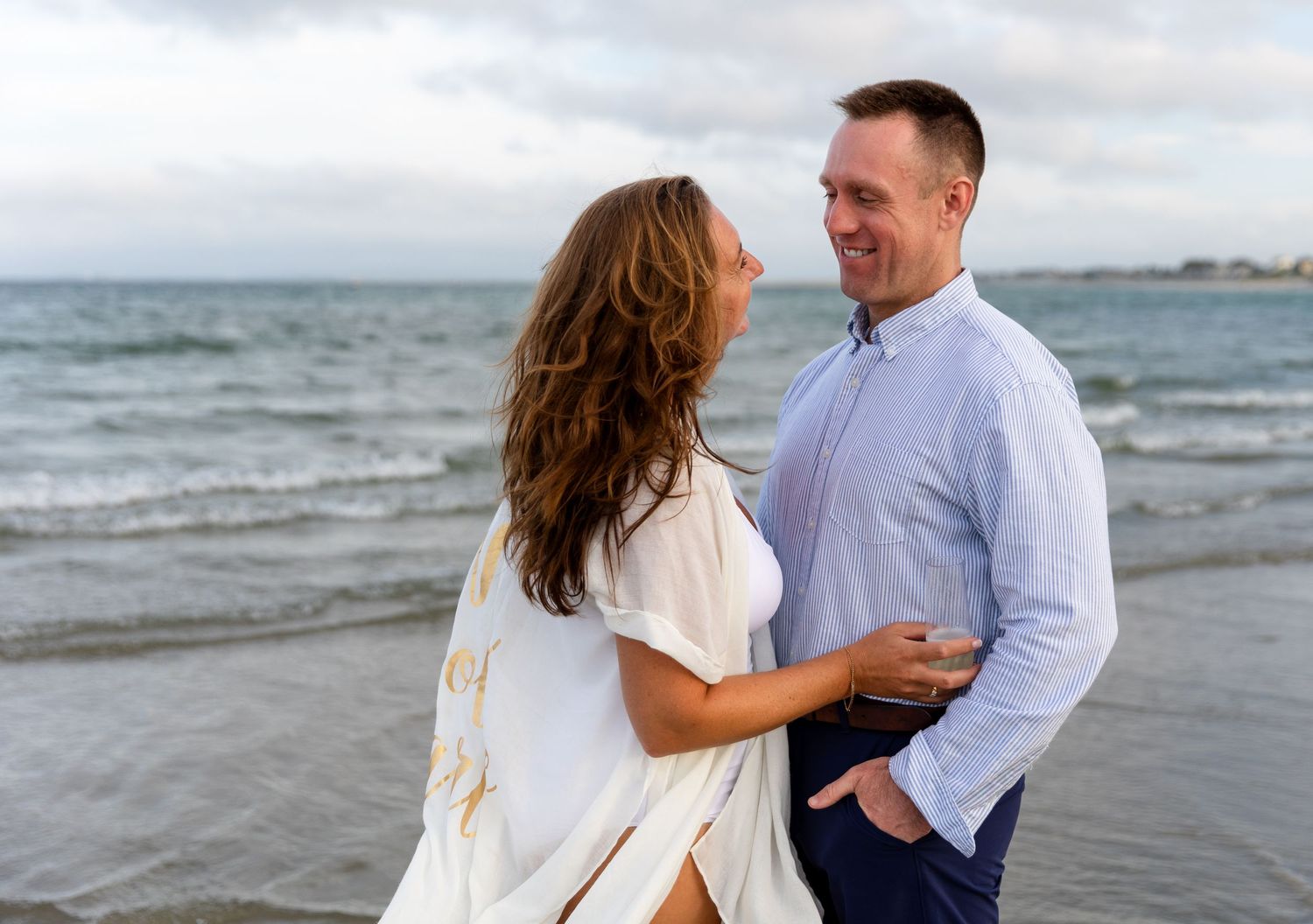 A couple shares a romantic moment together by the ocean on a cloudy day while walking along the beach.
