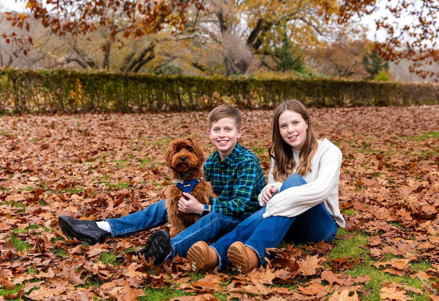 Family lying on autumn leaves wearing coordinated outfits during golden hour photo session in park.