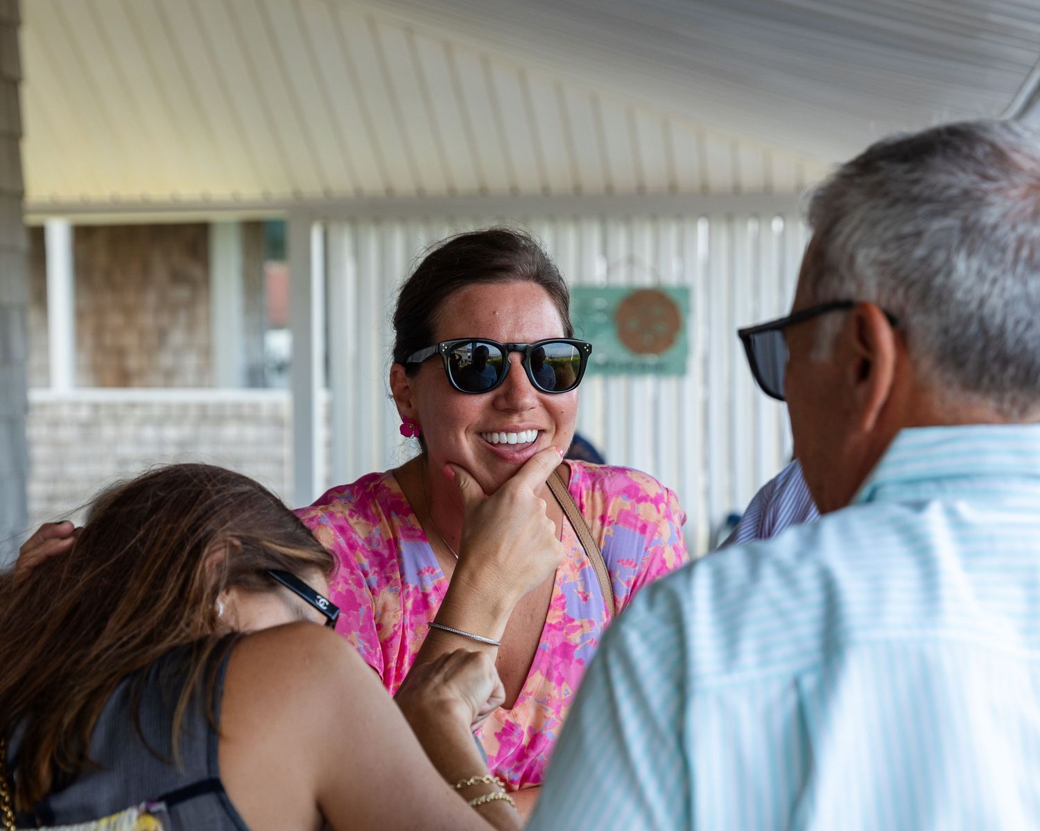 A person in pink floral attire laughs joyfully while interacting with others outdoors.