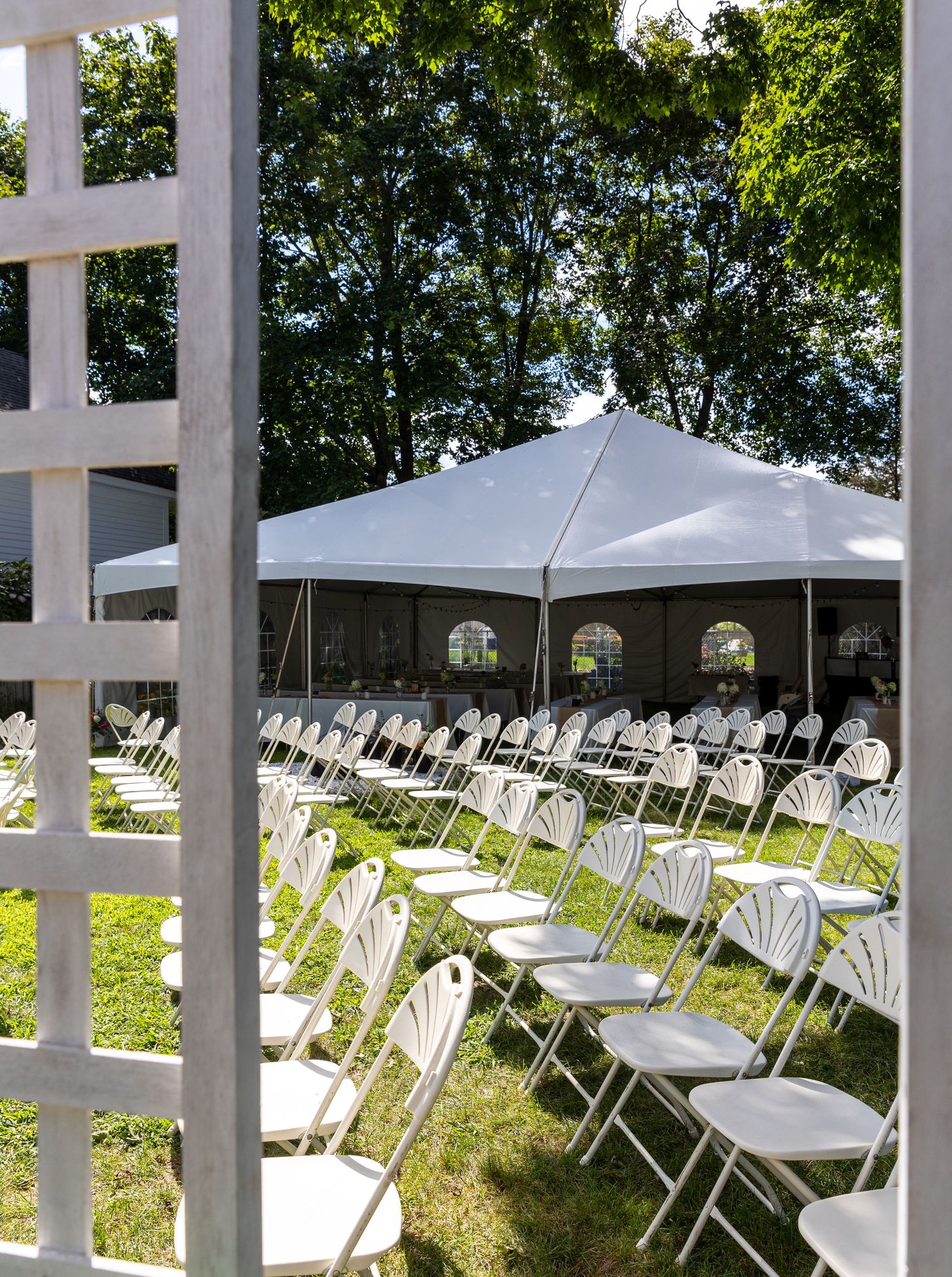 Rows of white folding chairs arranged outdoors under tall trees for an outdoor ceremony or event.