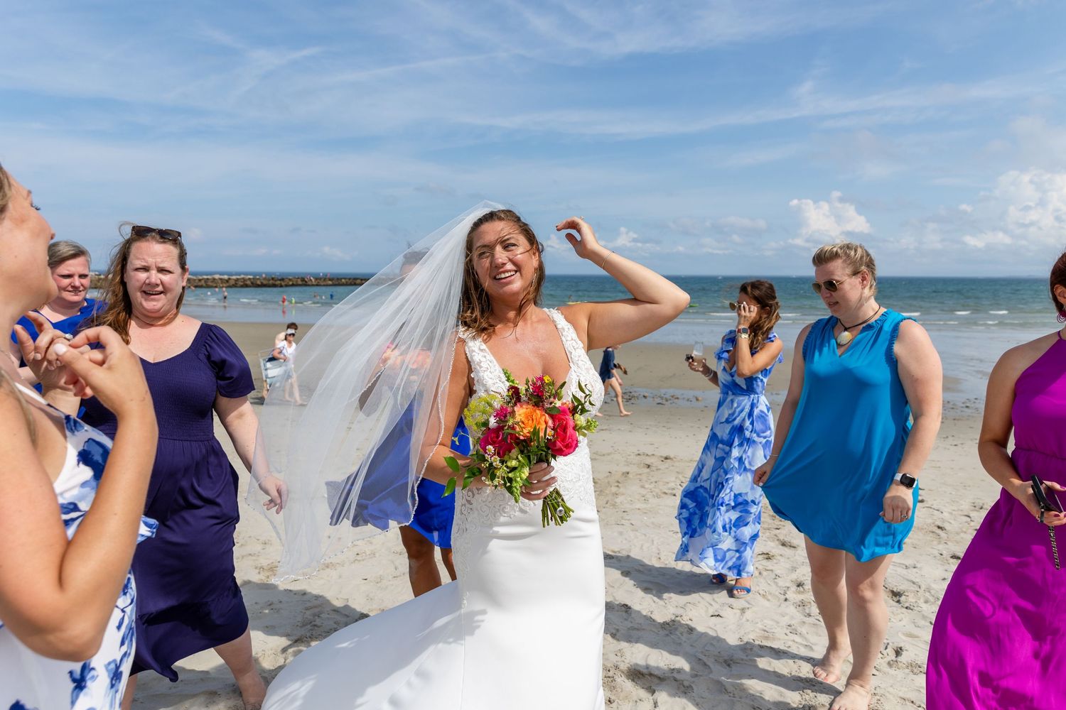 A group of people celebrating and having fun together at a sunny beach wedding with blue skies and ocean views.