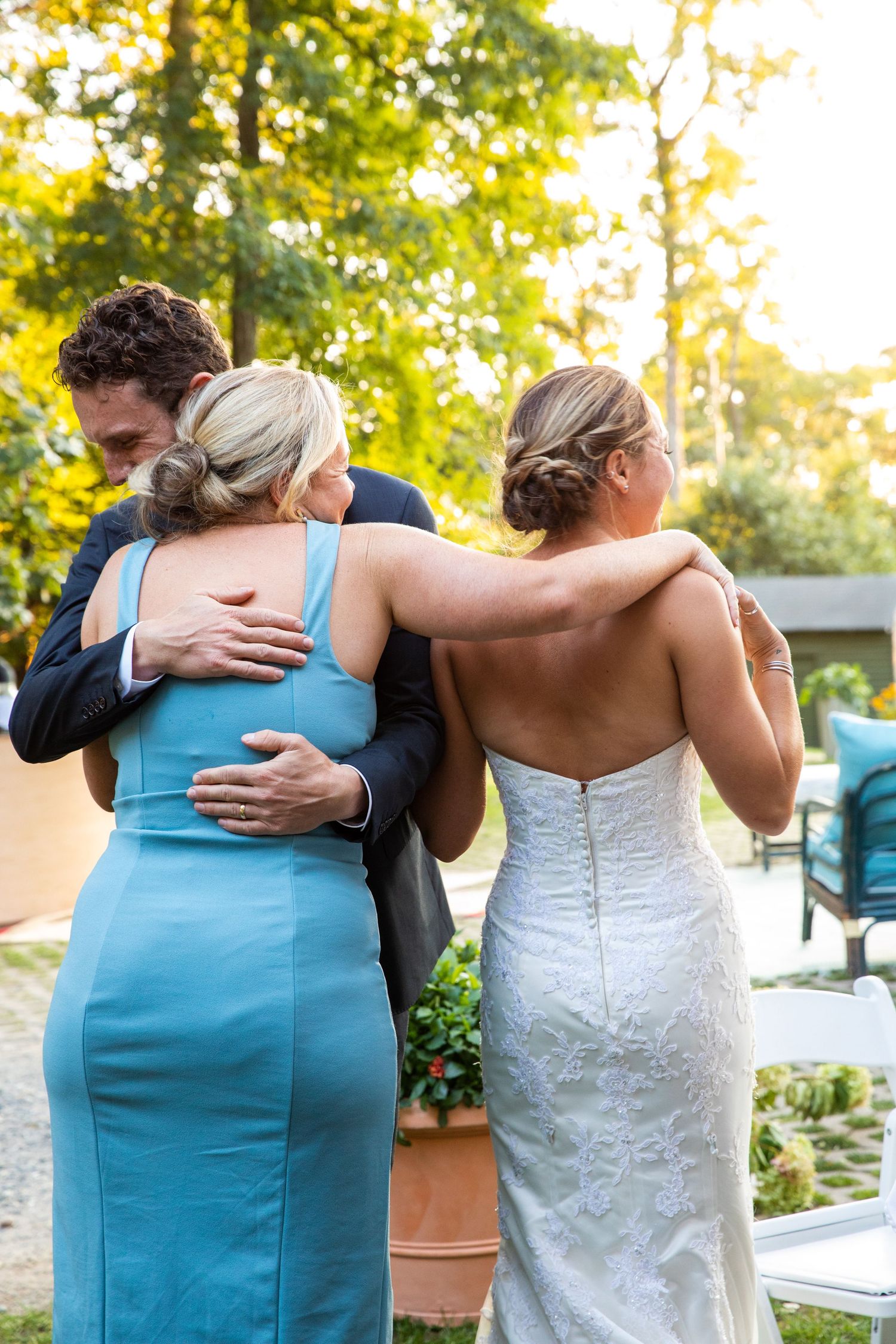 Two people in wedding attire embrace in tender moment outdoors during golden hour lighting.
