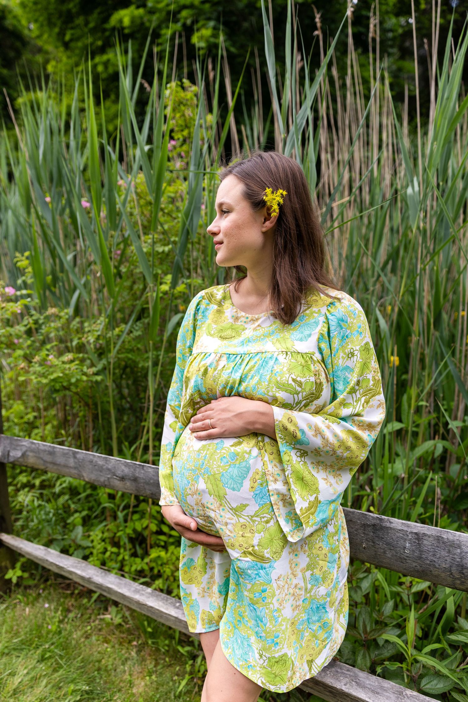 Someone wearing a floral yellow and blue patterned bohemian blouse poses against lush green garden vegetation.