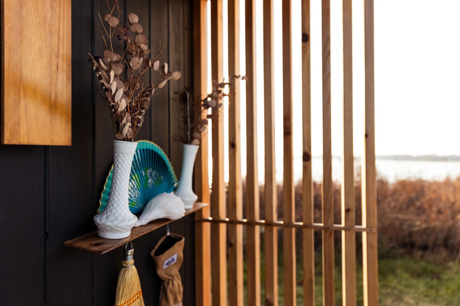 A turquoise ice skate sits on a wooden shelf against a black wall with vertical wooden slats and dried flowers.