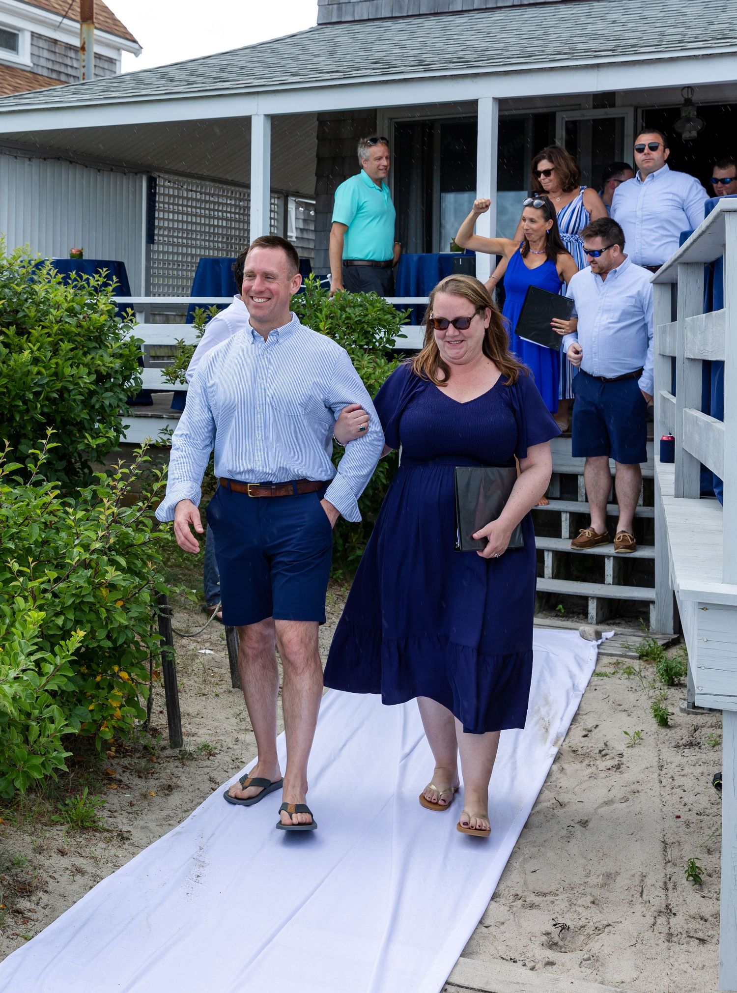 People are navigating white wooden walkways over sand during what appears to be a beach outing.