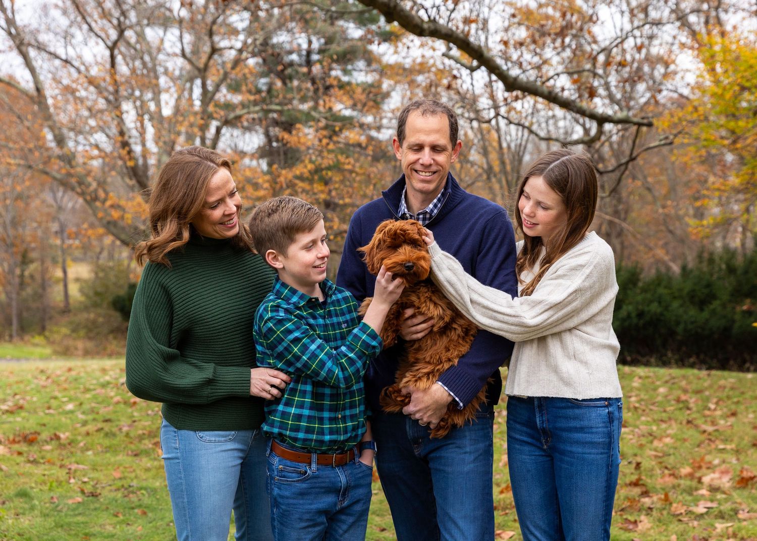 Family wearing blue and green outfits share candid moments together during outdoor autumn photoshoot in wooded setting.