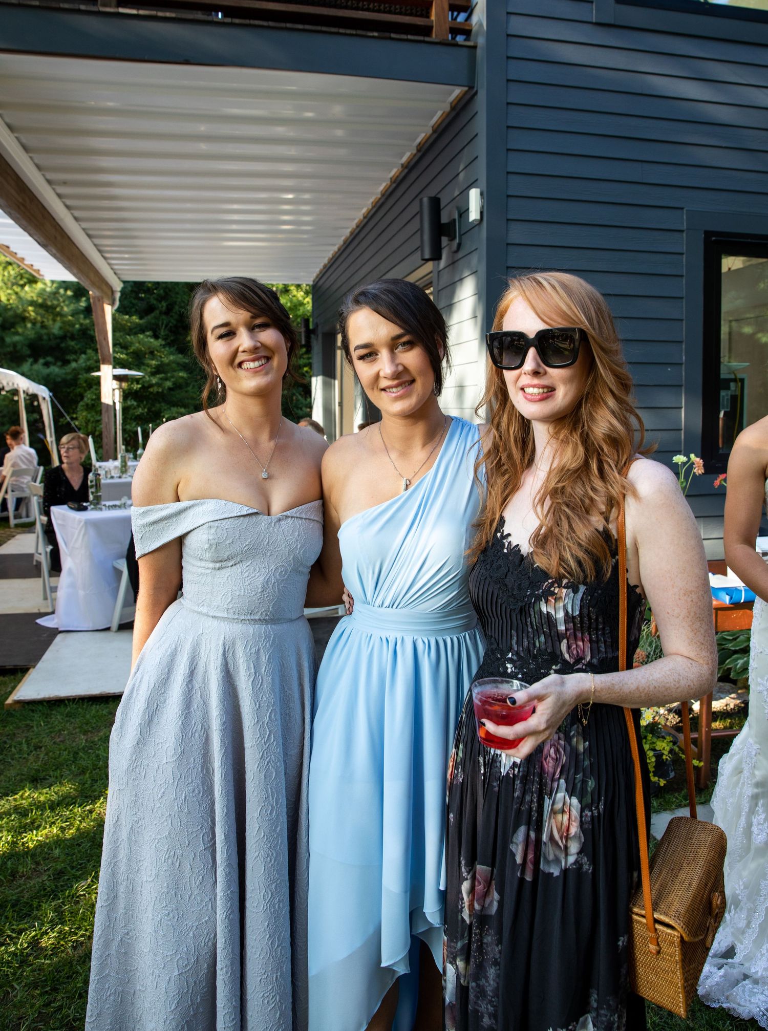 Several people gathered at an outdoor event wearing light blue and gray formal dresses in a summer setting.