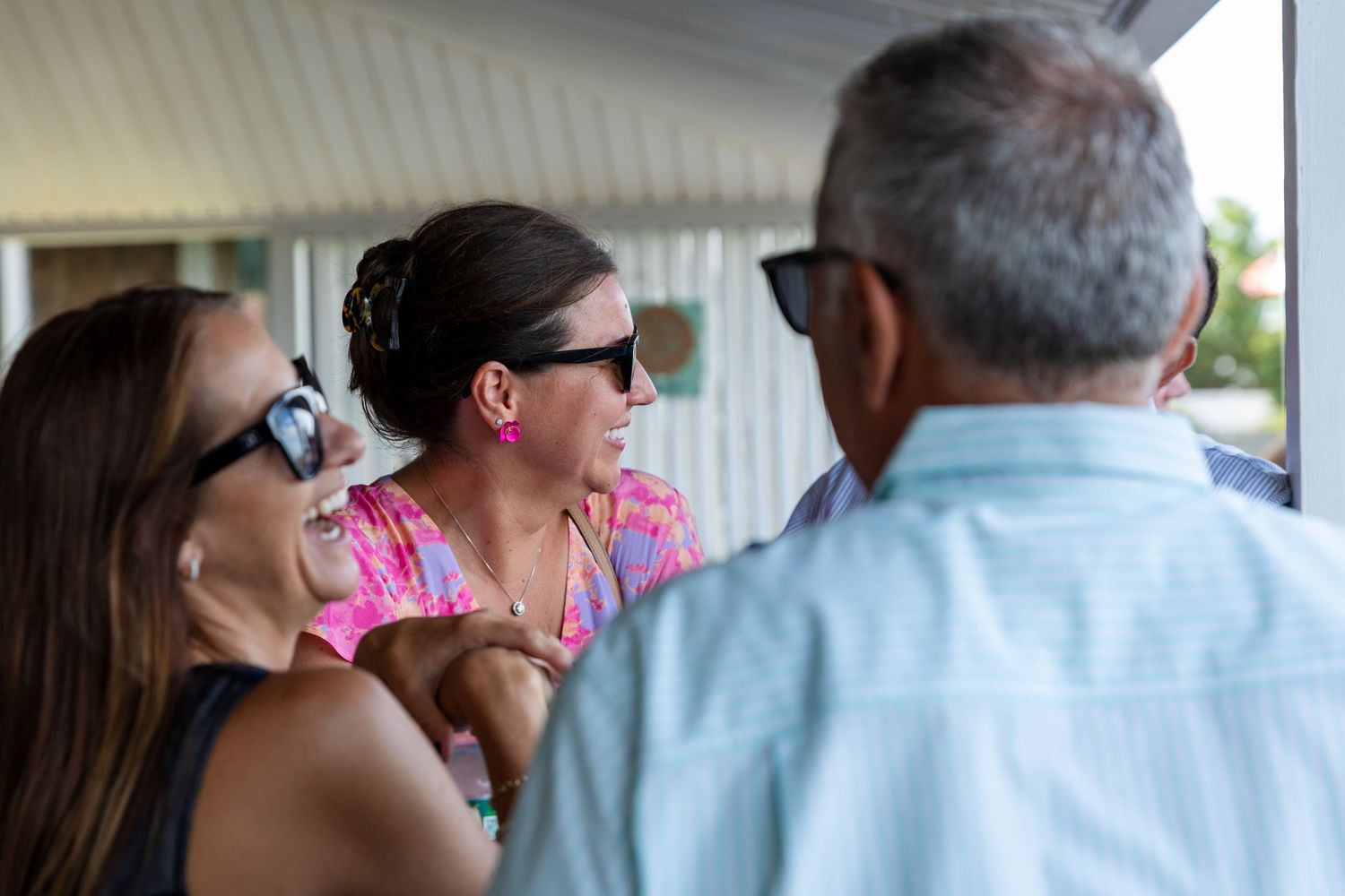 Three people engaged in casual conversation on a covered porch.
