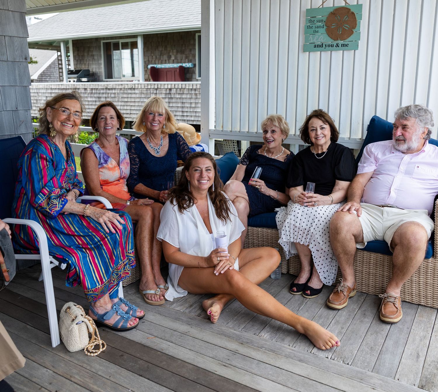 A group of people relaxing together on a covered porch with white siding on a summer day.