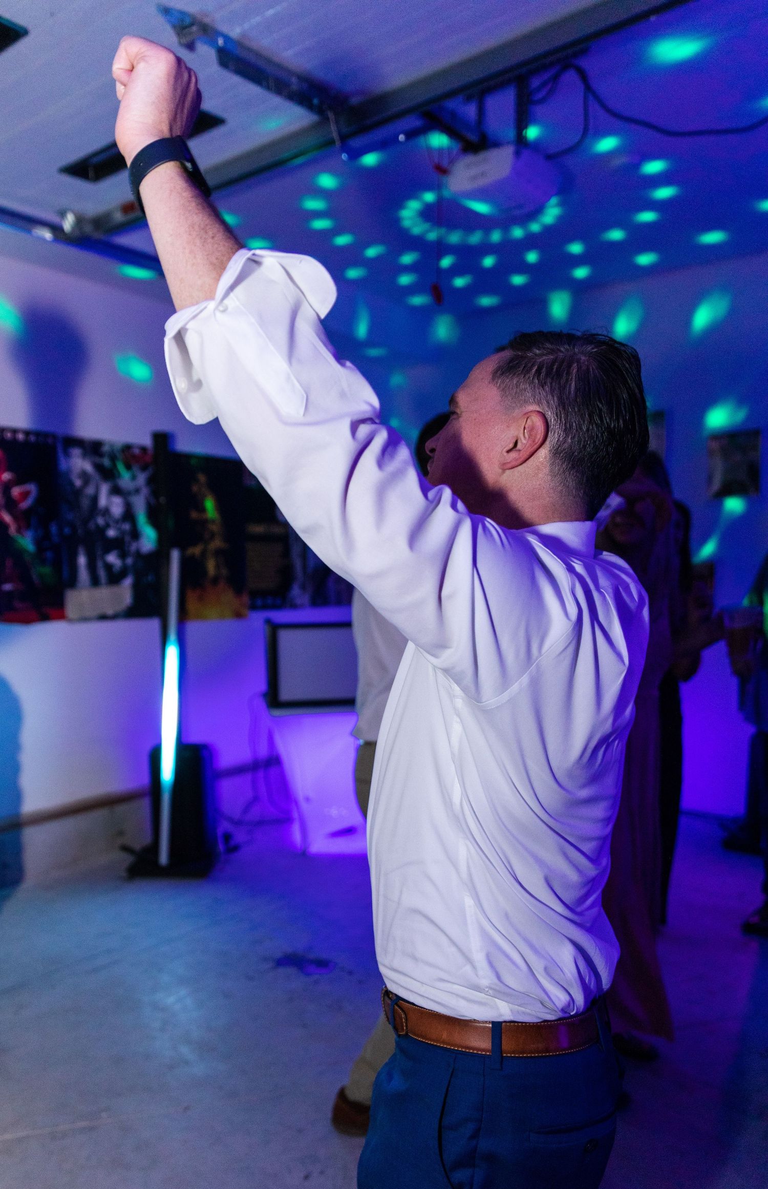Person in white dress shirt dancing under blue and purple disco lights in a party venue.