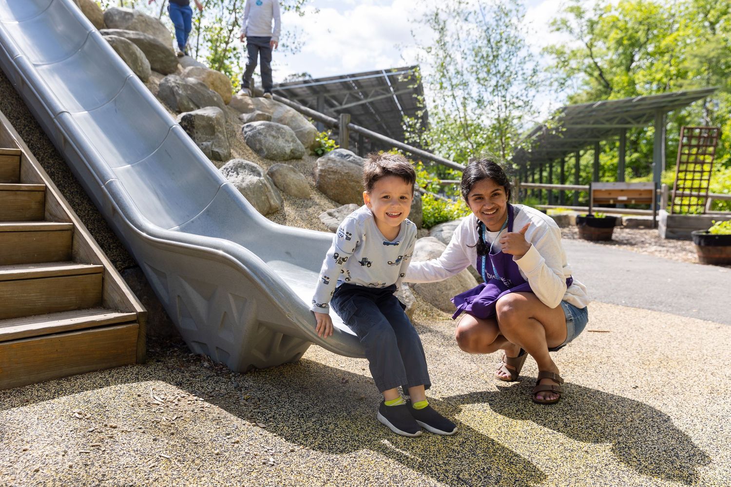 A metal slide extends from a playground structure with gravel and greenery visible in the background.