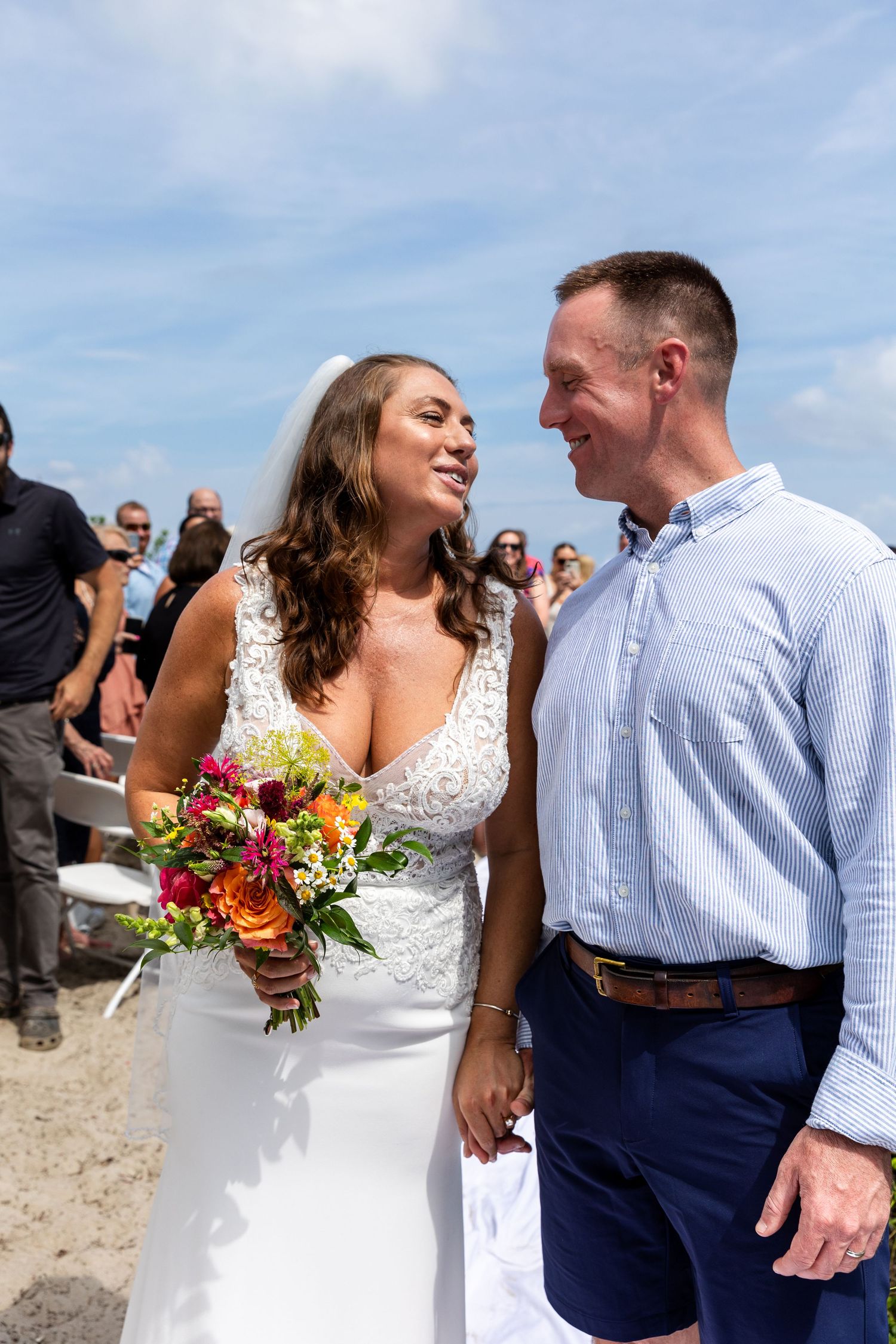 Newlywed couple shares a joyful moment outdoors during their beach wedding ceremony as bride holds vibrant bouquet.