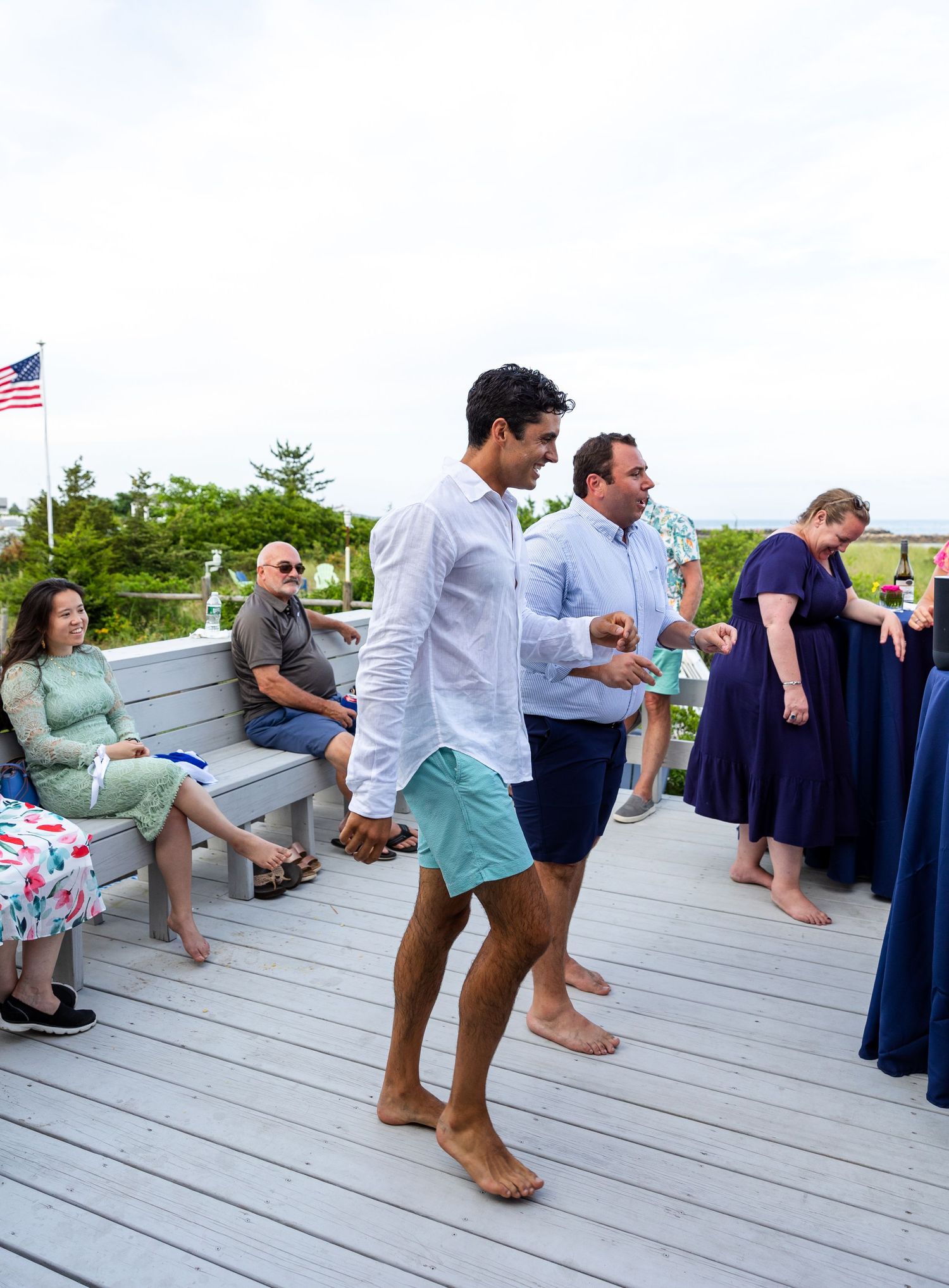 A group of people sitting in a row on wooden deck chairs arranged at a waterfront deck during a social gathering.