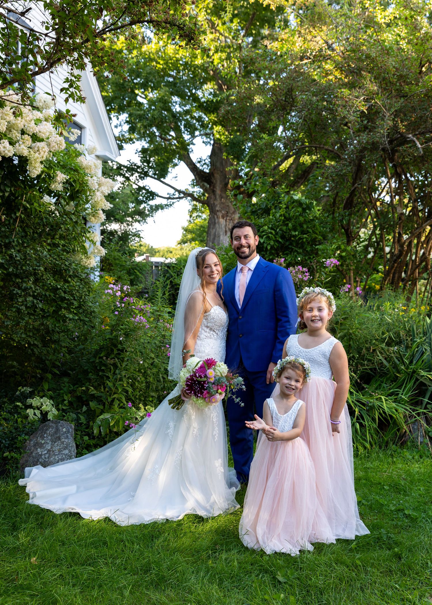 A wedding couple and young attendants pose together on a grassy path with trees in the background during golden hour.