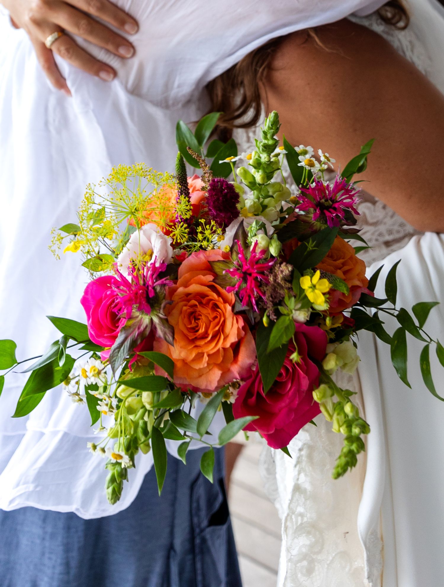 Vibrant bridal bouquet featuring orange roses, hot pink flowers, and mixed wildflowers against white fabric.