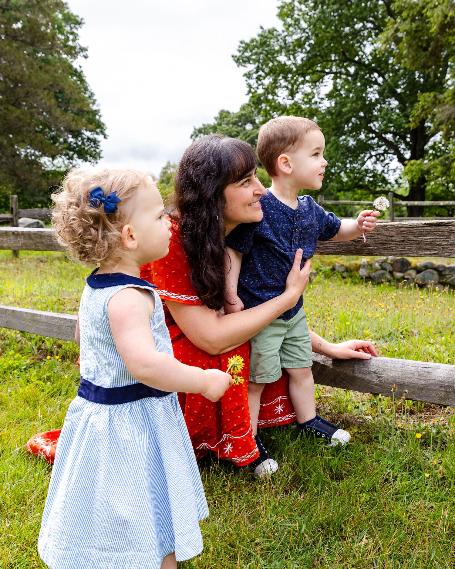 Family enjoying a sunny day outdoors together by a wooden fence in a grassy field on a summer afternoon.