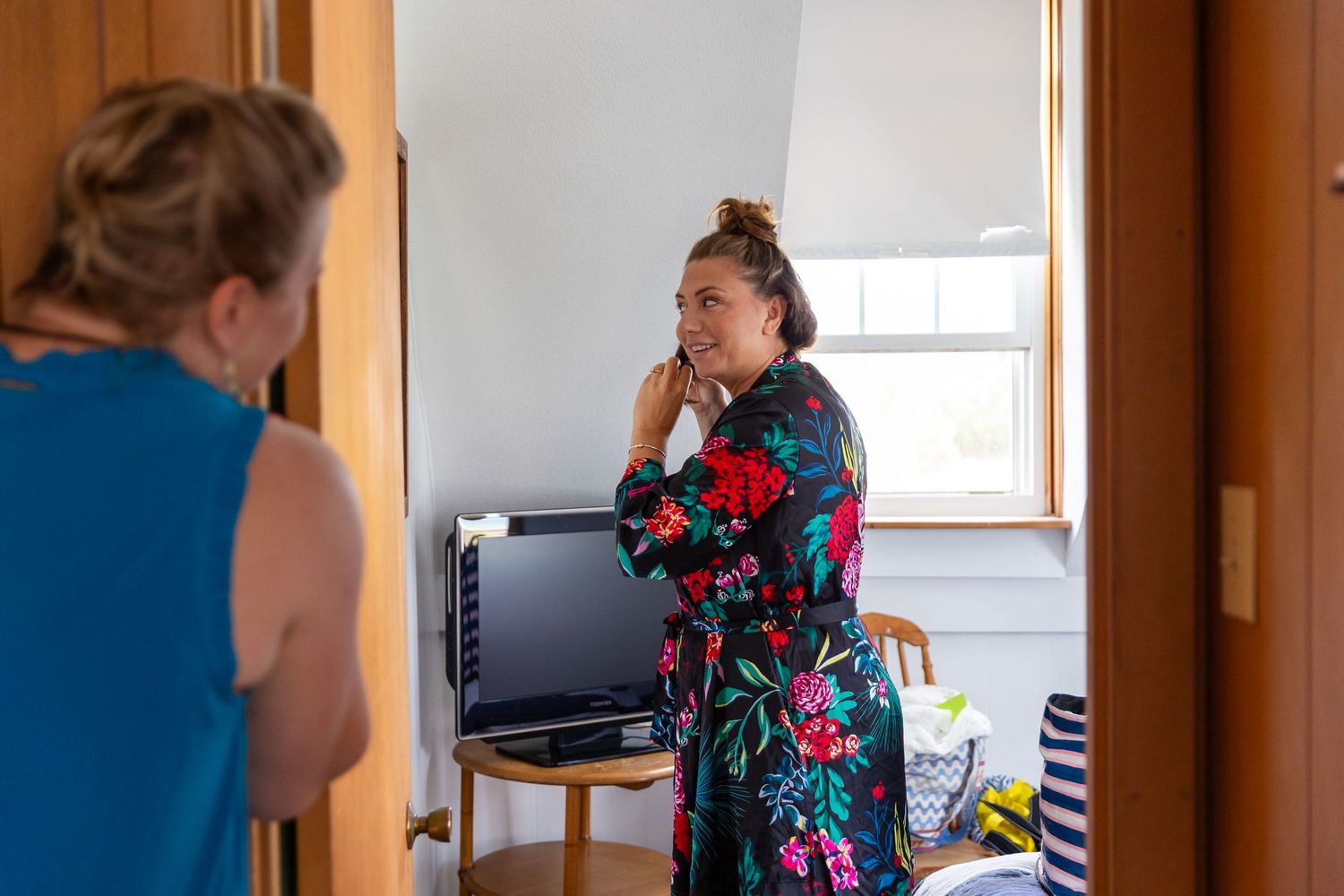 Two individuals interact in a casual living space, with one wearing a colorful floral robe near a window.