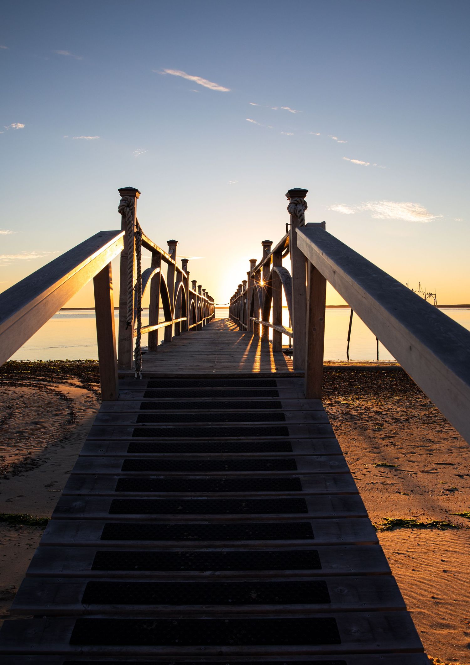 Wooden pier with white railings stretches into the distance during golden hour sunset.