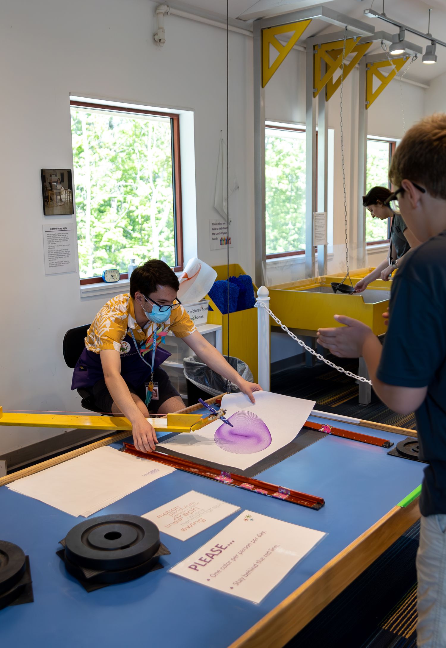 People working at a lab table with colorful paper sheets and equipment in a well-lit room with windows.