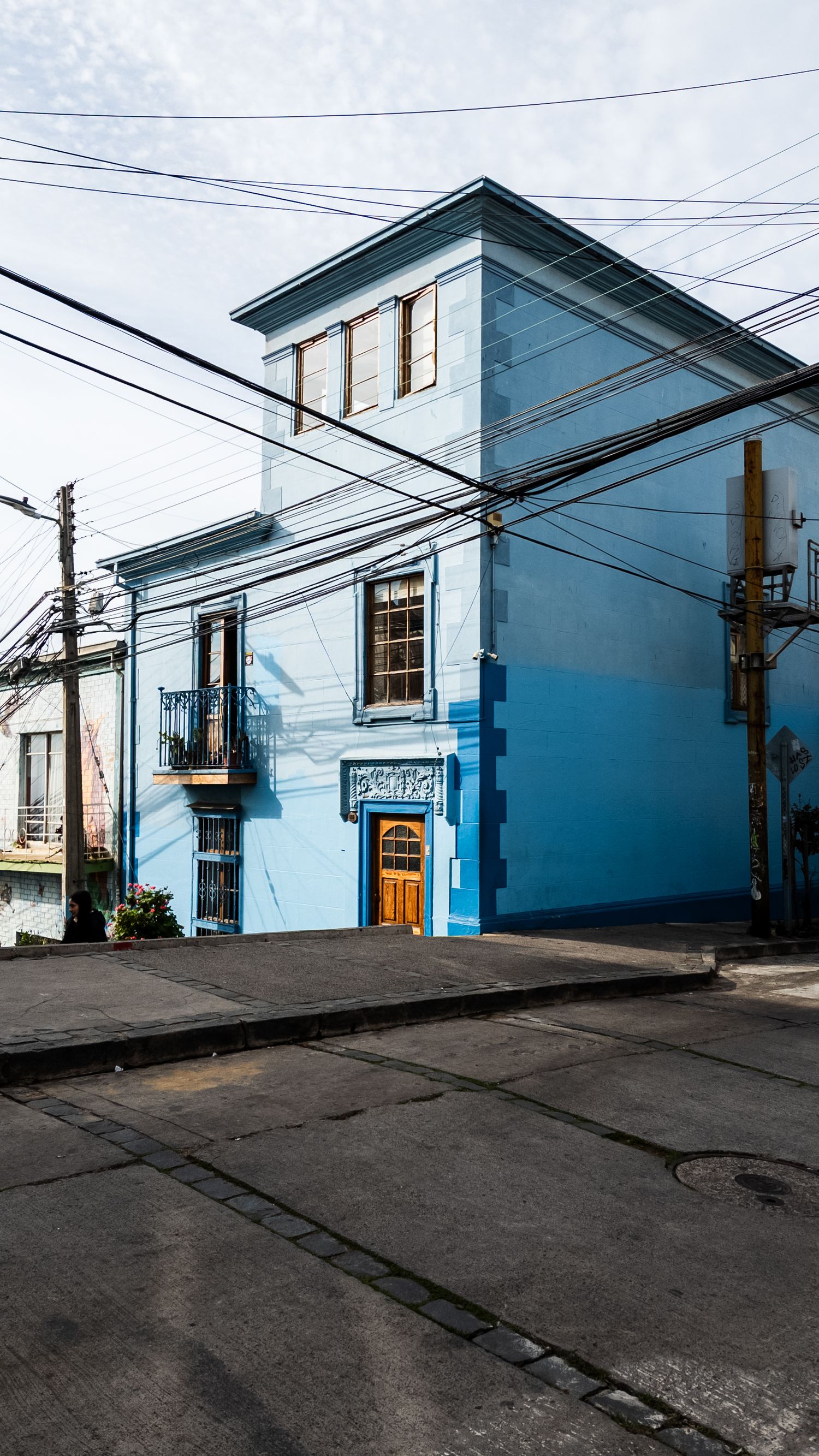 A series of blue and white corner buildings along a steep urban street with power lines and telephone poles overhead.