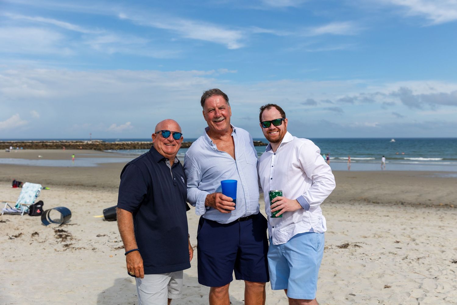Three people enjoying a sunny day together on a beach with waves and blue sky in the background.