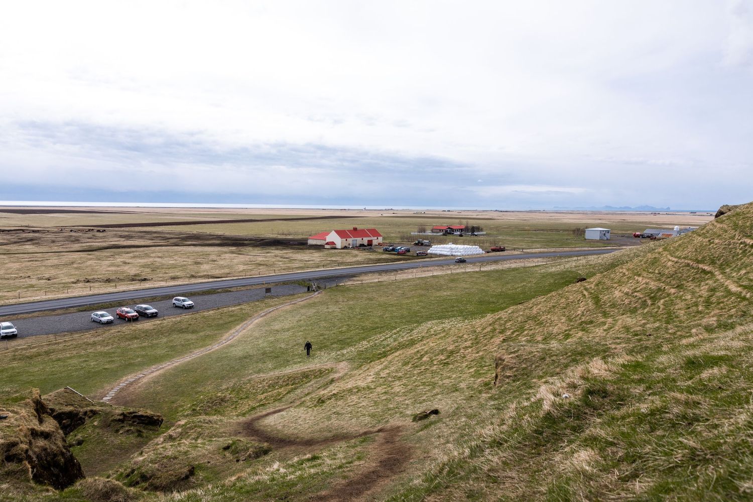 Scenic view of a coastal road with scattered buildings and grassy hills in rural Iceland.