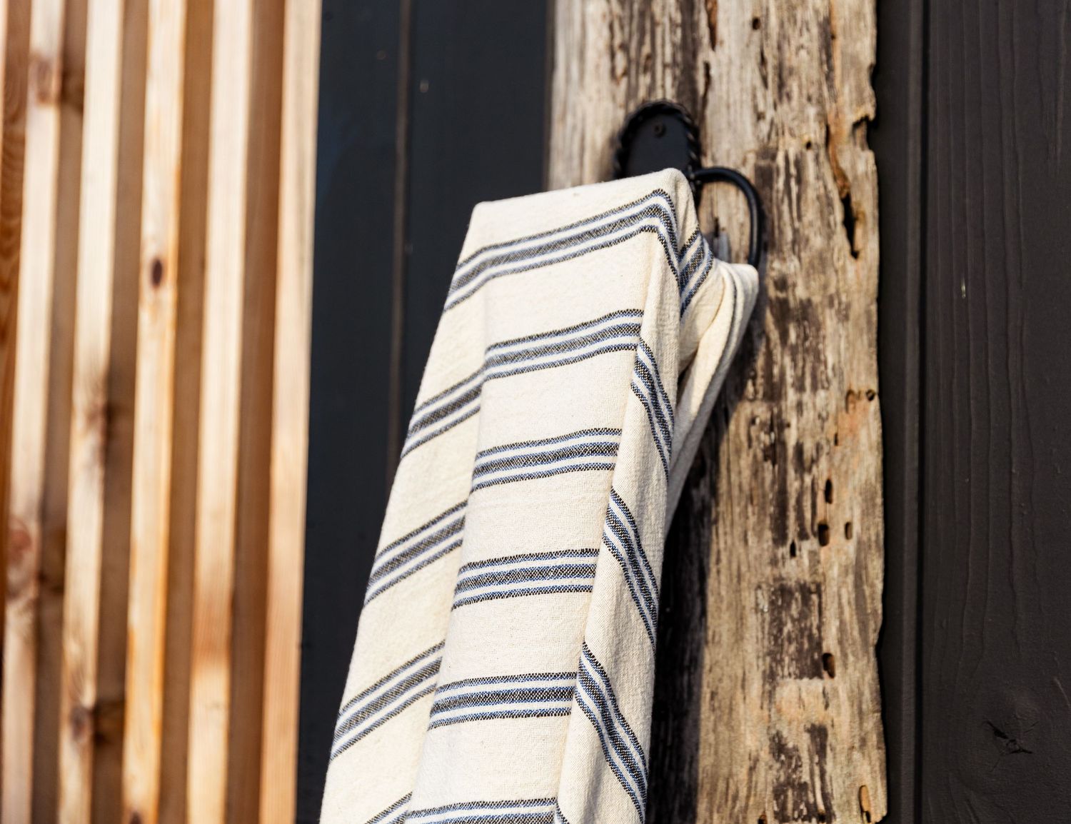 Clean white and navy striped towels hang neatly on rustic wooden posts against a dark background.