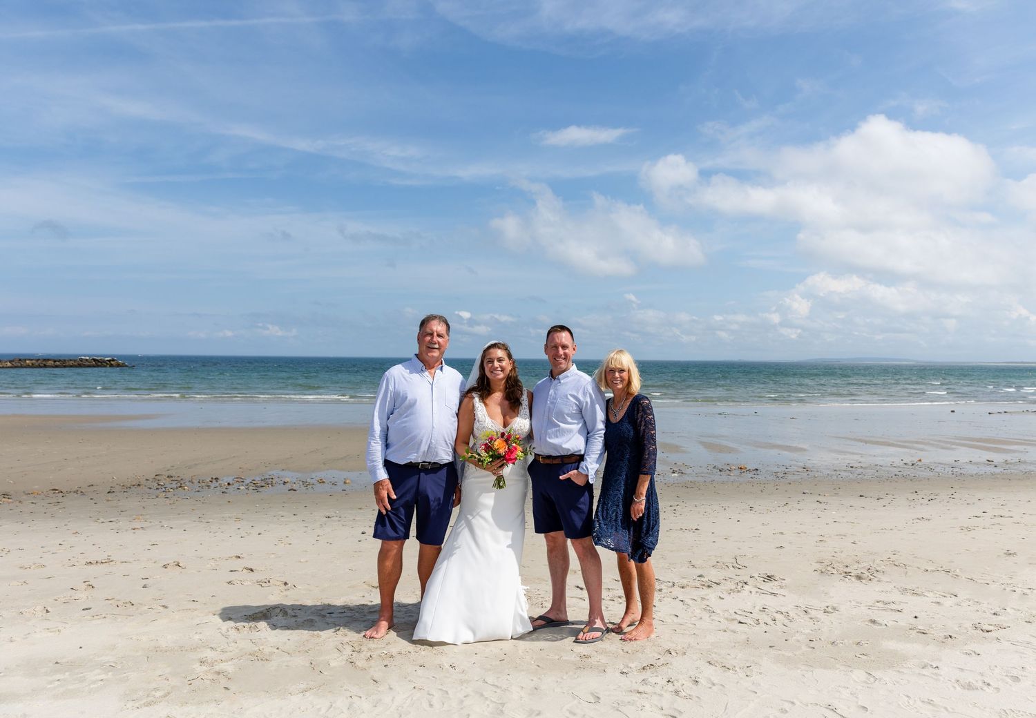A small group stands together on a sunny beach with calm ocean waters and blue skies in the background.