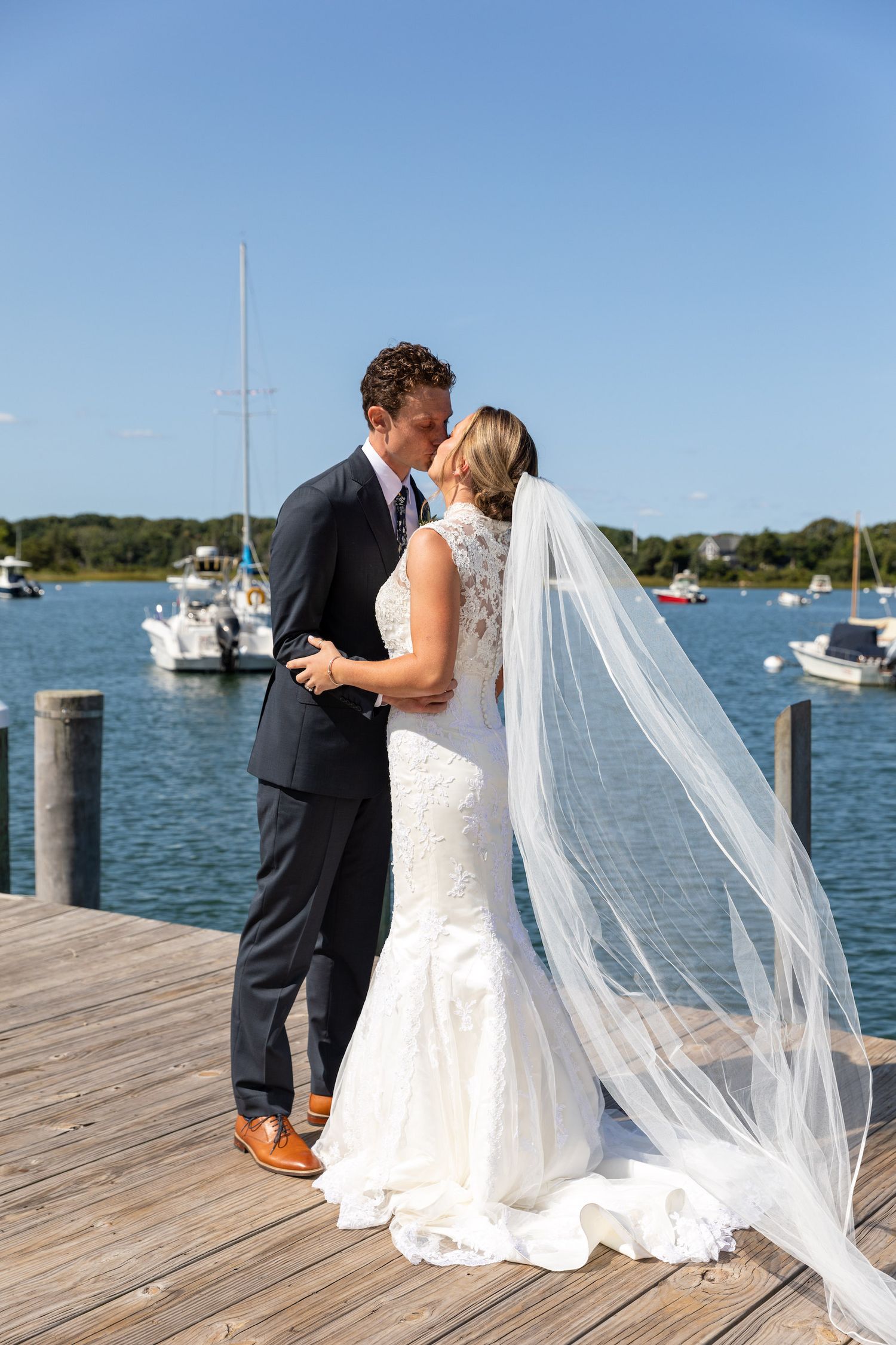 A wedding couple shares an intimate moment on a wooden dock overlooking a marina with sailboats in the background.