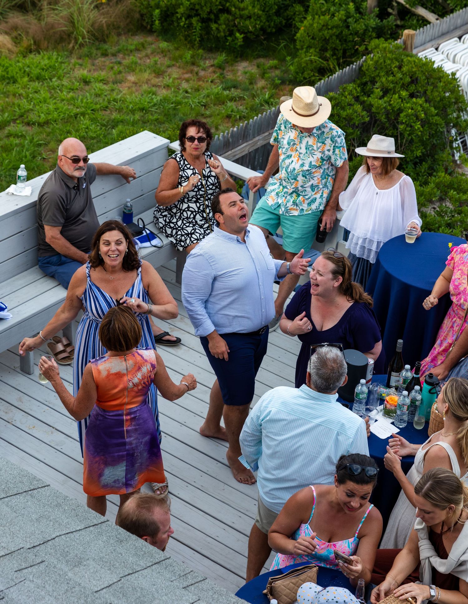Group of people gathered on an outdoor deck for a social event with drinks and summer attire.