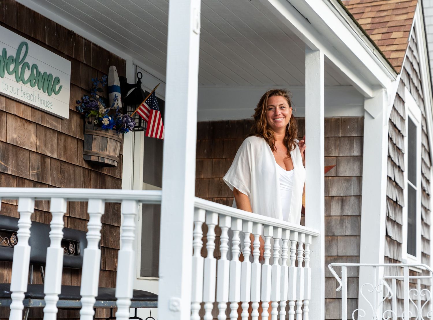 A row of white wooden rocking chairs lines a covered porch of a traditional American home with white columns.