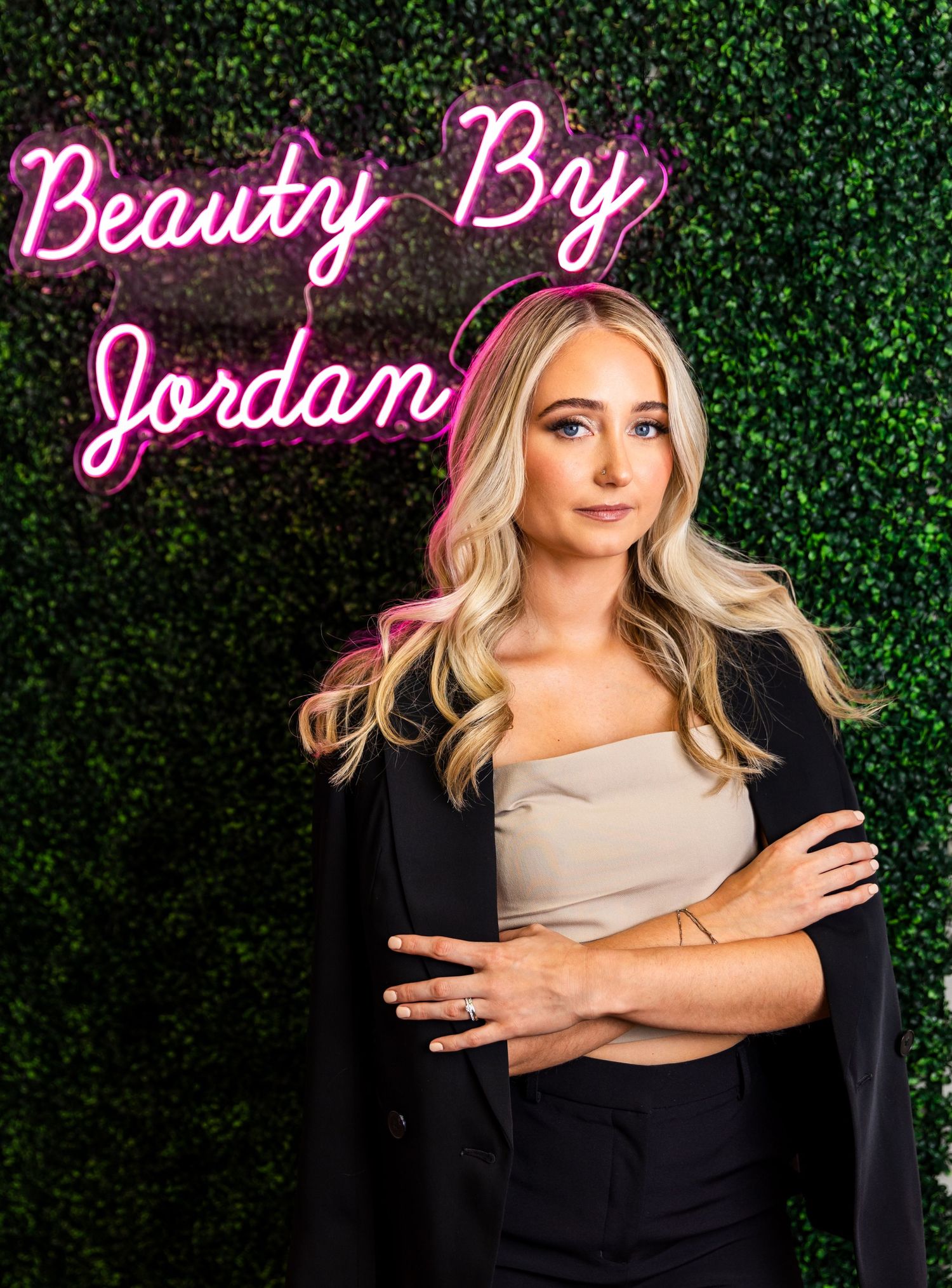 A beauty salon storefront with pink neon signage reading 'Beauty By Jordan' against a green hedge wall background.
