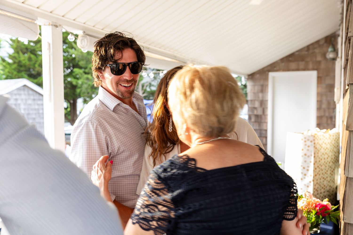 A group of people gather outdoors at a covered patio area for a social event on a sunny day.