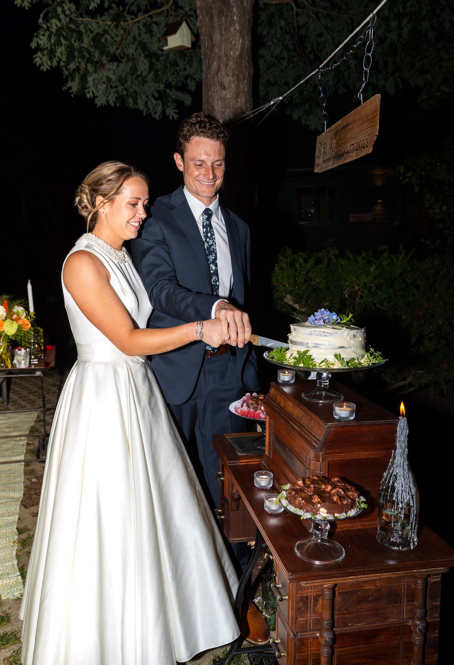 Two people in wedding attire interacting with a vintage wooden piano bar during an evening reception celebration.