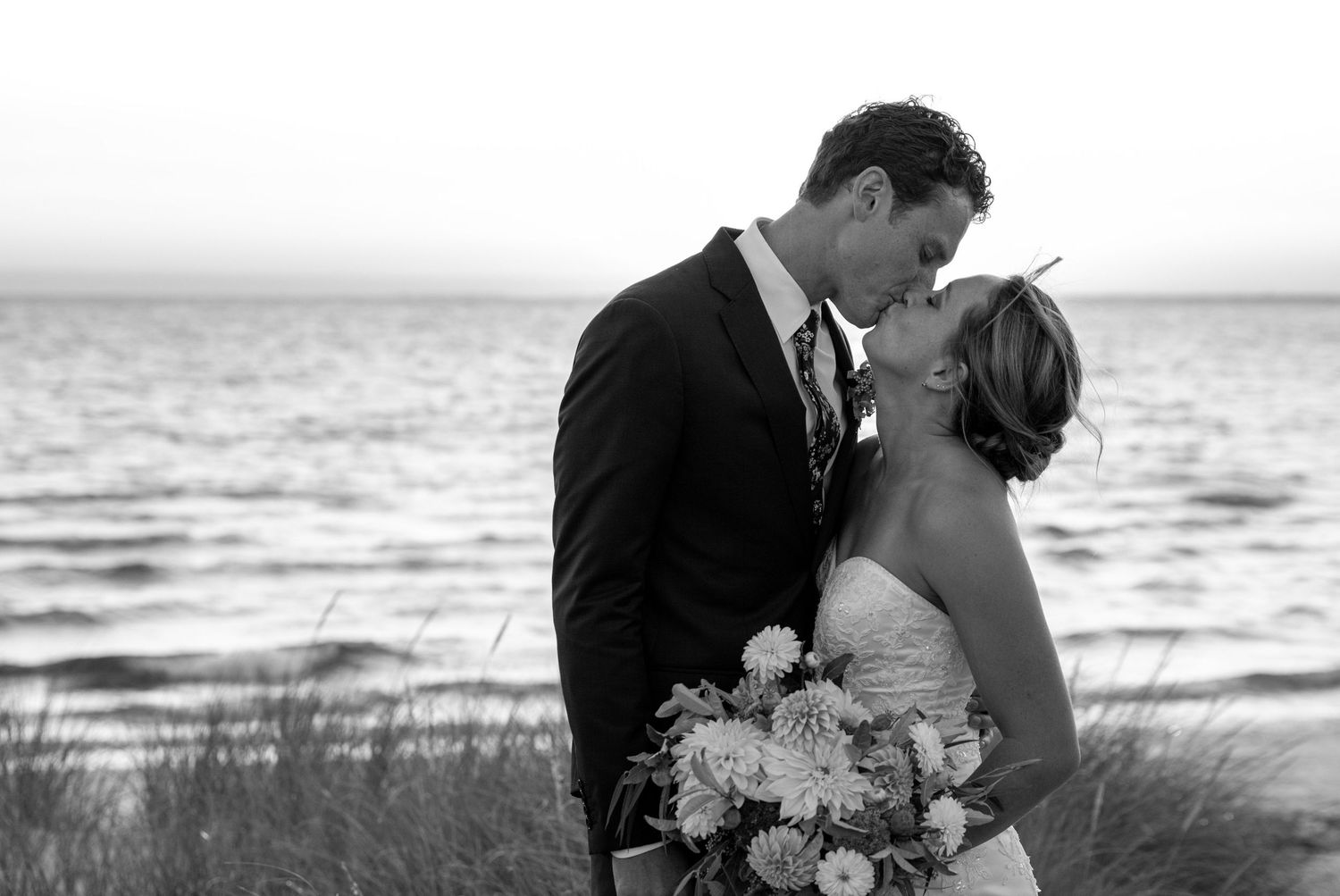 A romantic black and white wedding photo series showing silhouettes of a couple embracing on a beach during sunset.