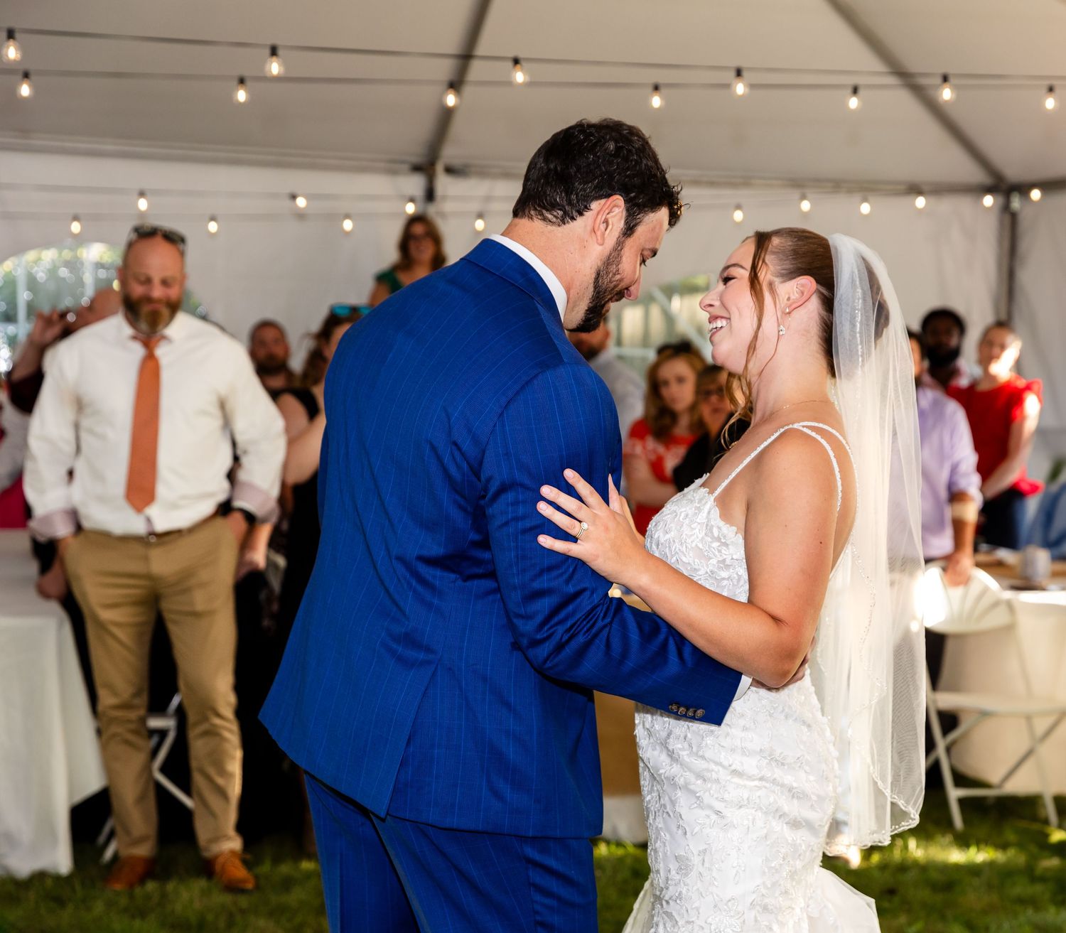 A couple shares an intimate first dance moment under a white wedding tent with string lights overhead.