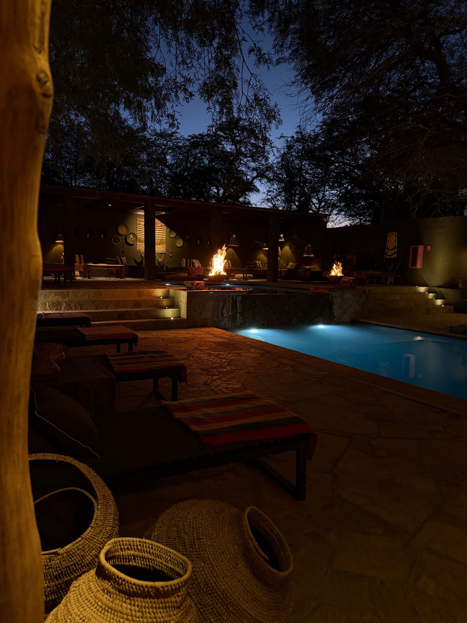 A dimly lit swimming pool area at night with illuminated torches and lounge chairs creating a serene atmosphere.