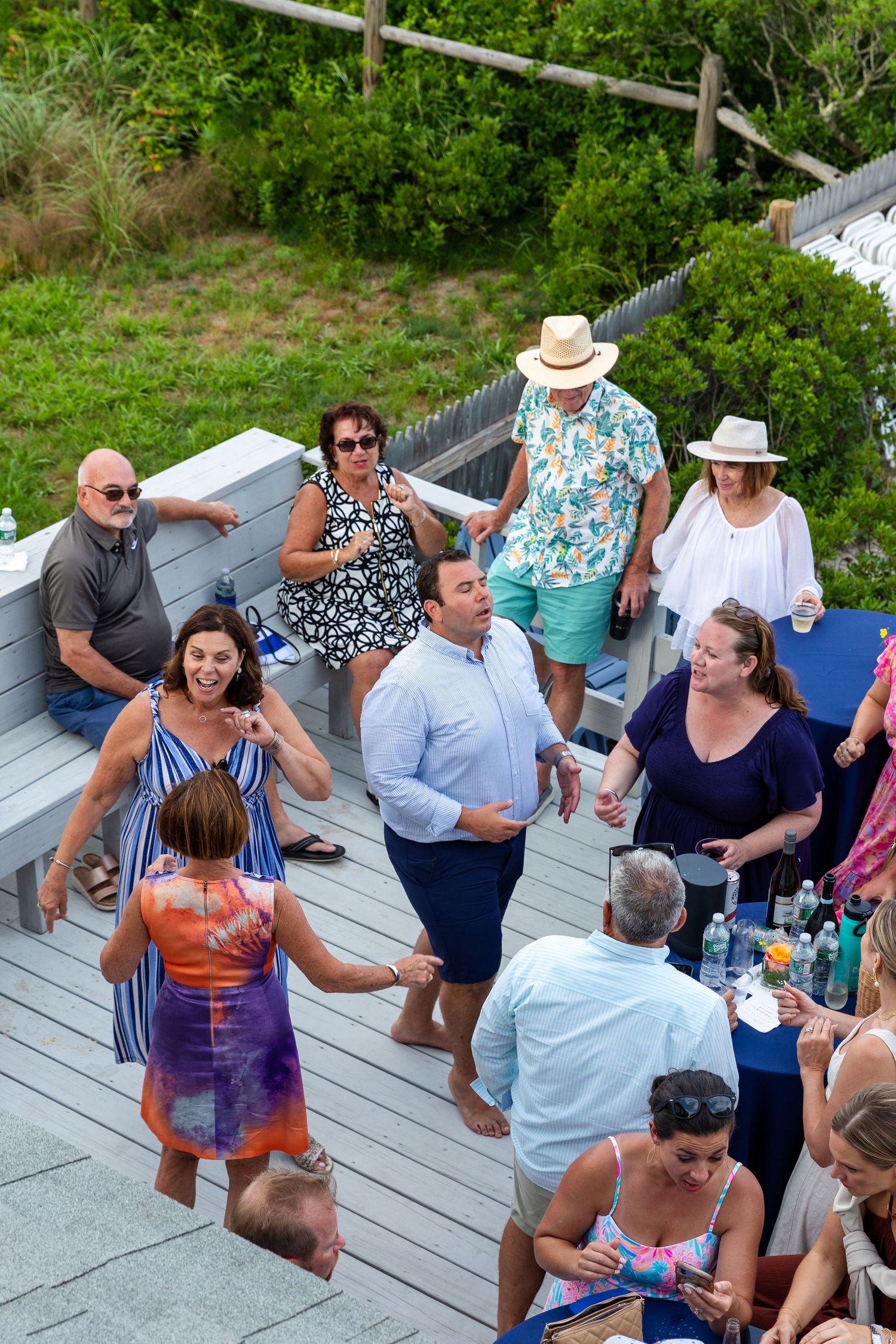 People gathered on a wooden deck for an outdoor summer party with drinks and casual attire.