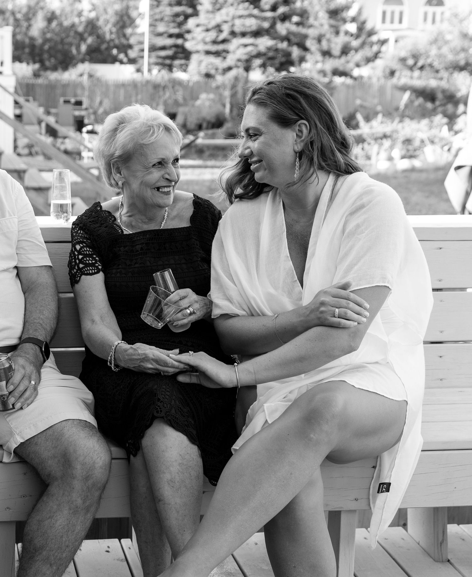 A candid black and white photo of two people sitting on a bench outdoors sharing a joyful conversation.