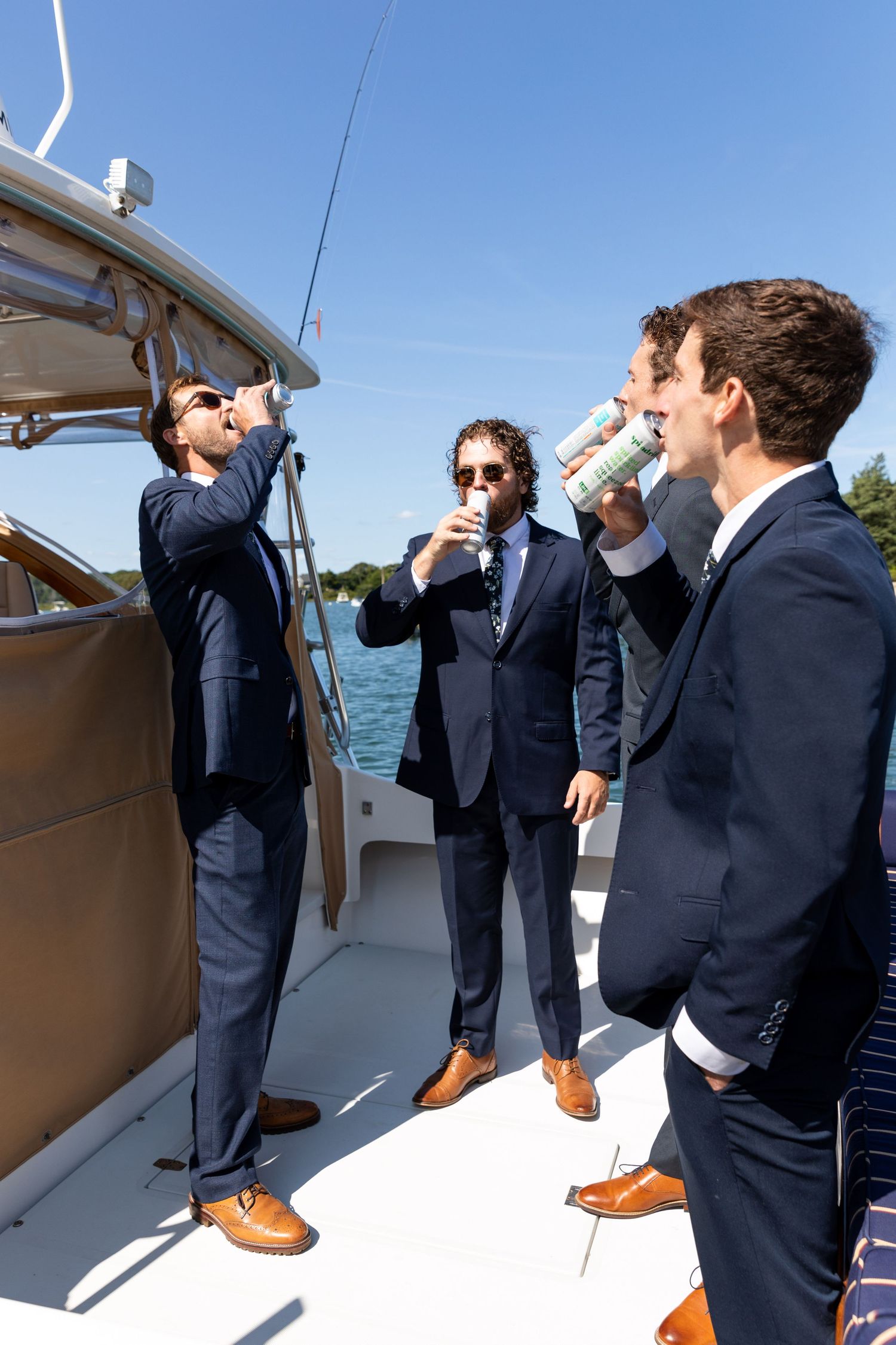 A group in navy suits dance in a sequence of playful jumping poses aboard a boat deck on a sunny day.