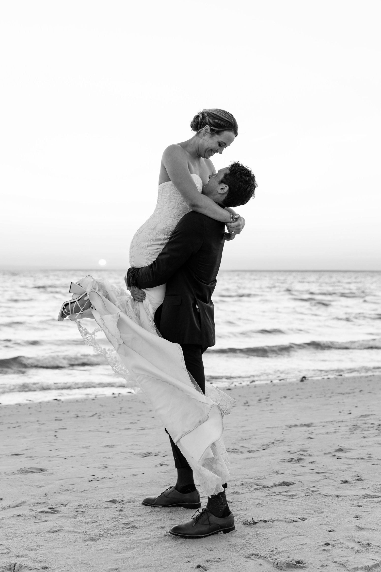 A romantic black and white beach photo of a couple embracing, with the ocean waves in the background.