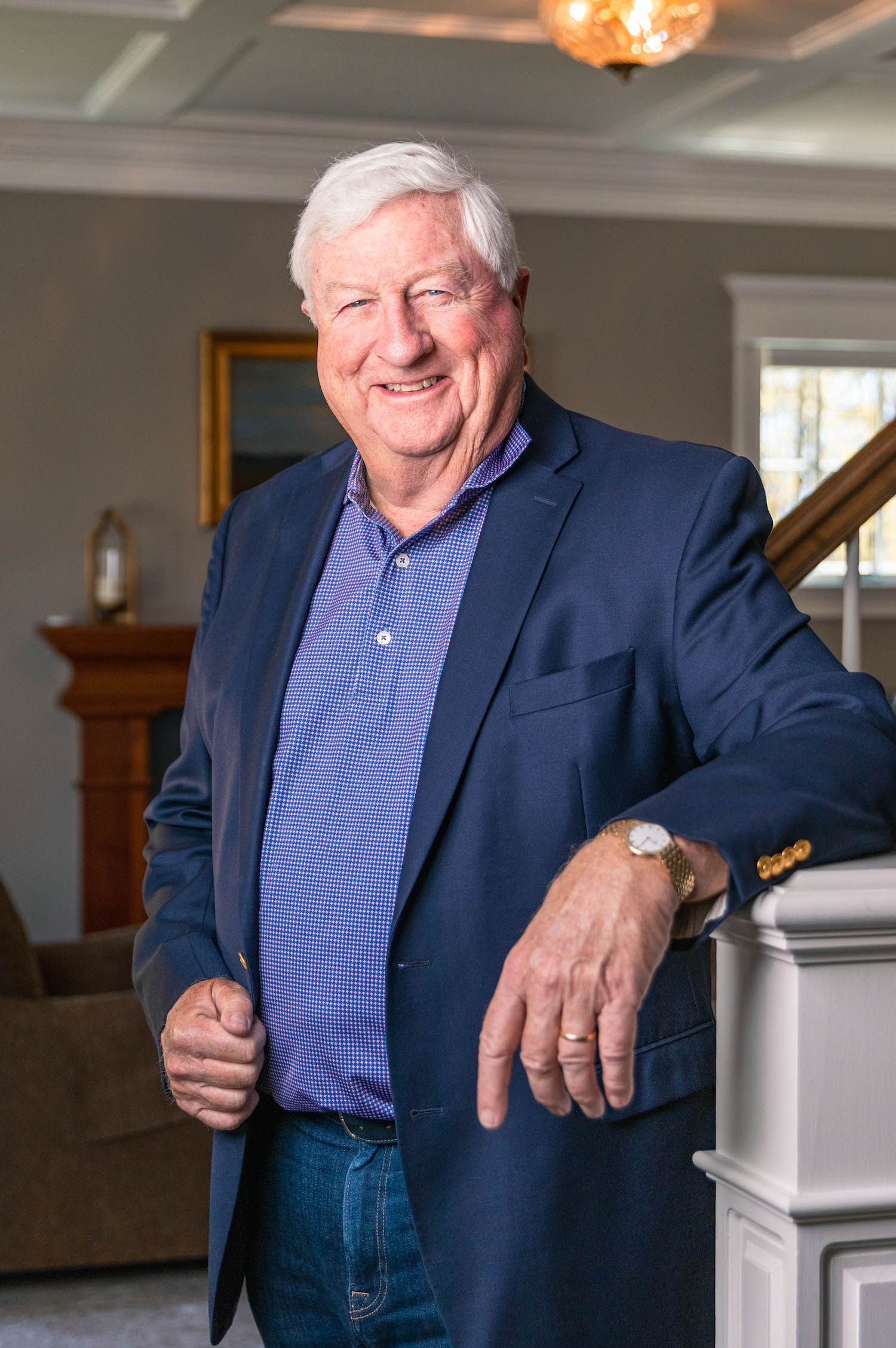 Professional senior executive in navy blazer and purple polo shirt poses in elegant home interior.
