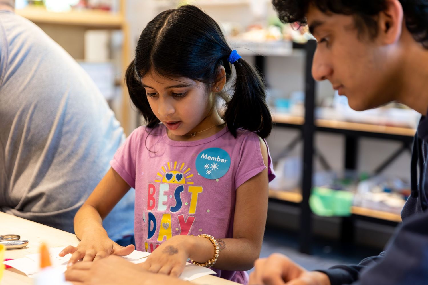 Students work together on educational activities in a classroom setting while gathering around tables and workstations.