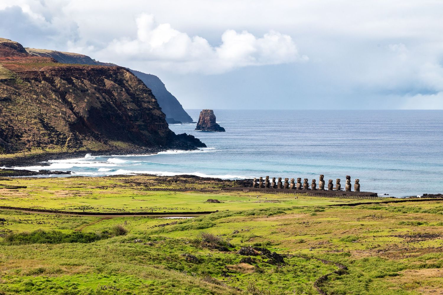A scenic coastal view of Easter Island (Rapa Nui) with stone Moai statues standing against dramatic cliffs and blue ocean waters.