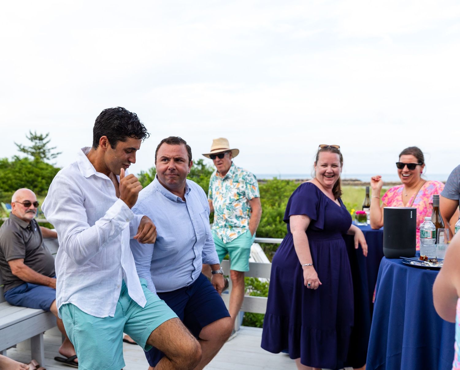 Party guests mingle and dance together at an outdoor celebration with blue decor and festive atmosphere.